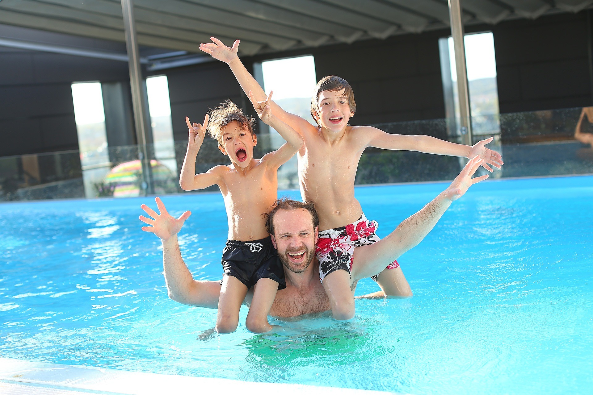 Deux enfants sur les épaules de leur père dans une piscine